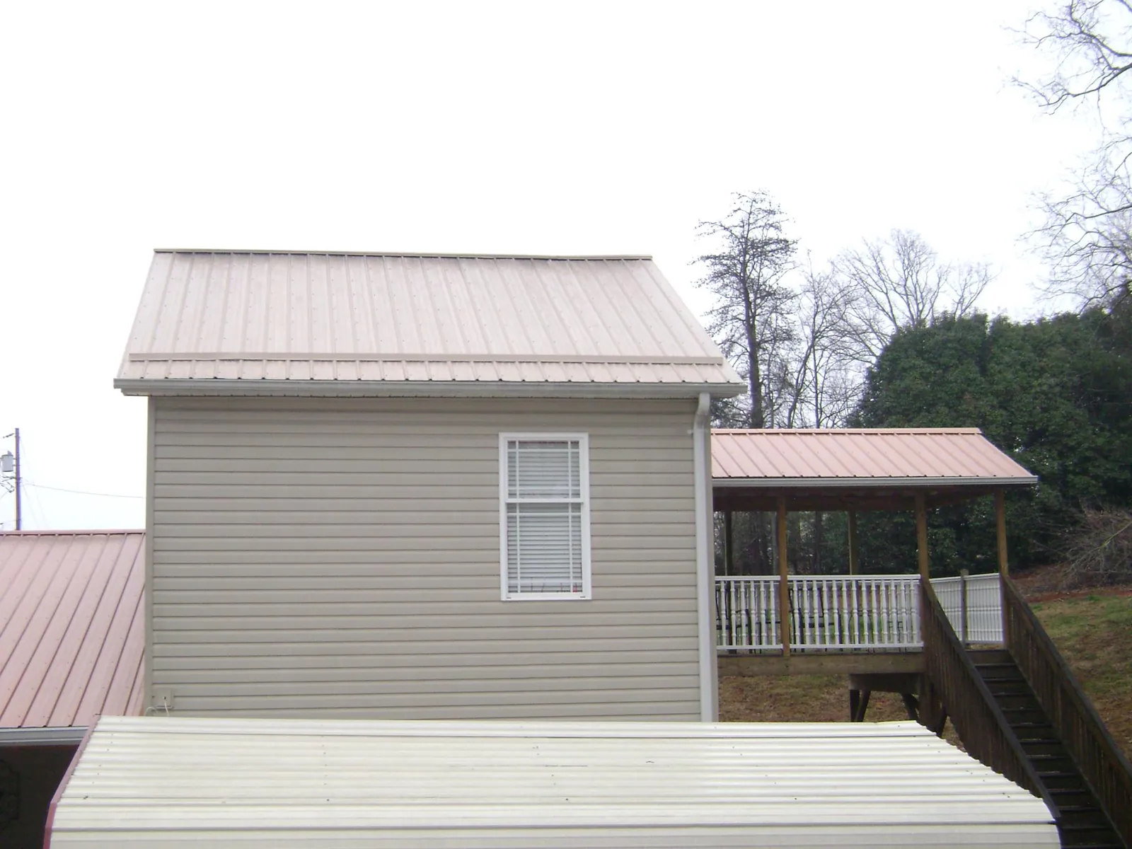 Tan metal roofs on a two story addition and attached porch, from a Roof Replacement job in Albion